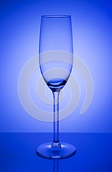 Empty champagne glass on a mirror with spot in blue background