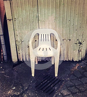 Empty cheap white plastic chair in grungy alleyway.