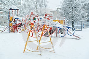An empty children`s playground in the courtyard of high-rise buildings during a snowfall.