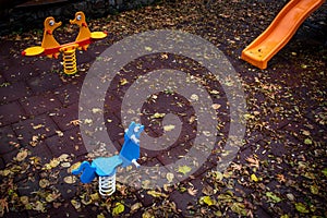 Empty childrens playground with colourful toys and leaves on the ground