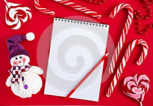 Empty Christmas wish list blank with candies and snowman on red background. Top view, mockup