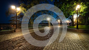 Empty city park landscape at the late evening or night with lit lightposts and brick road