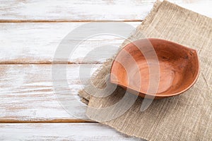 Empty clay brown bowl on white wooden background and linen textile. Side view, copy space