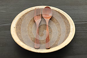 Empty clay dish with wooden cutlery on the black table