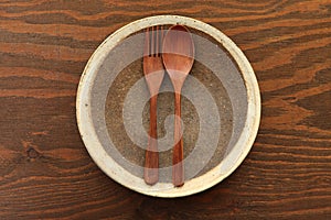 Empty clay dish with wooden cutlery on a dining table