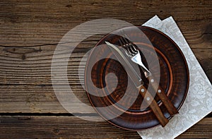 Empty clay plate, cutlery, napkin on wooden background. Table setting captured from above. Top view, flat lay. Rustic style. Copy