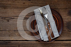Empty clay plate, cutlery, napkin on wooden background. Table setting captured from above. Top view, flat lay. Rustic style. Copy