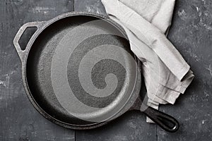 Empty, clean black cast iron pan or dutch oven top view from above on black table with towel