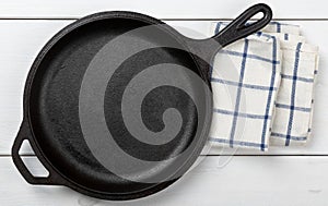 Empty, clean black cast iron pan or dutch oven top view from above on white table with towel