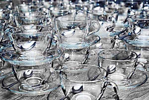Empty clean glass transparent cups with saucers, teaspoons on gray wooden table. Catering, tea party preparation concept