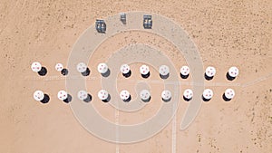 An empty clean sandy beach with two rows of parasols and cabanas, aerial view.