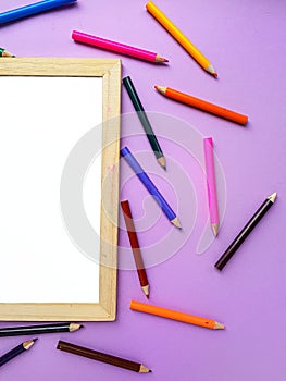 Empty clean white sheet for the buyer`s text on the purple background and school supplies, pencils. Back to school.