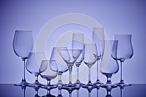 Empty clear glassware. Set of glasses for different alcoholic drinks and cocktails on light violet  background