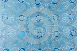 Empty clear plastic bottles with caps stacked on a blue background. Recycling and environment concept