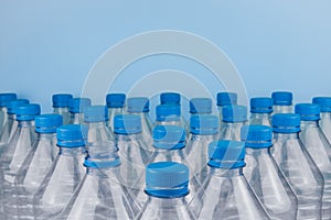 Empty clear plastic bottles with caps stacked on a blue background. Recycling and environment concept