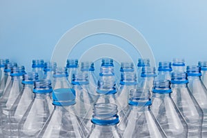 Empty clear plastic bottles with caps stacked on a blue background. Recycling and environment concept