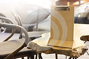 An empty clipboard stands on an unusual wooden table in a street cafe