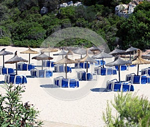 Empty closed beautiful beach with turned blue chaise lounges, deck chairs and straw umbrellas