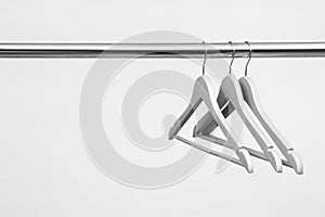 Empty clothes hangers on metal rail against light background