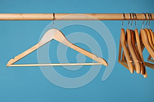 Empty clothes hangers on wooden rail against light blue background