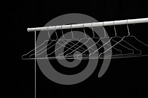 Empty coat hanger on a white bar, black background