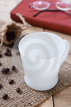 Empty coffee cup and coffee beans on sackcloth mat, selection focus