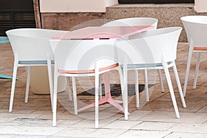 Empty coffee and restaurant terrace with pink table and white chairs. Cafe in the street. Summer terrace in Europe. Open air cafe