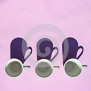 Empty coffee and tea cups stand in row on pink background in sunlight with shadows. Top view, flat lay. Minimal style. Art design