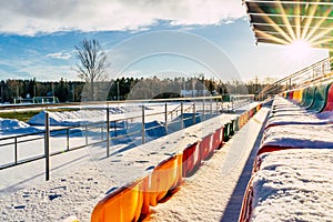 Empty Colorful Football & x28;Soccer& x29; Stadium Seats in the Winter Covered in Snow - Sunny Winter Day with Sun Flare