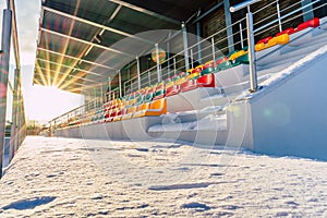 Empty Colorful Football & x28;Soccer& x29; Stadium Seats in the Winter Covered in Snow - Sunny Winter Day with Sun Flare