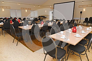 Empty conference room with projection screen, set tables and chairs