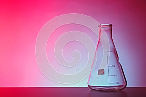 Empty conical flask on table against color background.