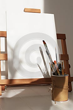 Empty copy space canvas on wood easel and paintbrush in artistic workshop interior