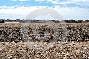 Empty corn field after fall harvest with residue over soil. Urban sprawl visible in the distance with residential