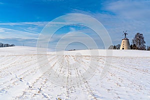 Empty Countryside Landscape in Sunny Winter Day with Snow Covering the Ground with Big Abandoned Windmill in Background