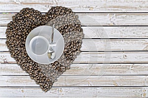 Empty cup of coffee and coffee bean hart drawing on white wooden table background