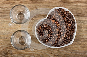 Empty cups, roasted coffee beans in white saucer in heart shape on table. Top view