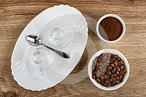 Empty cups, spoon in dish, bowl with roasted coffee beans, bowl with ground coffee on wooden table. Top view