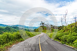 Empty curved asphalt road on green forest on mountain with cloudy sky