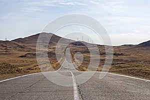 Empty curved cracked asphalt road to Lake Baikal is among the mountains with clear sky and dry grass.