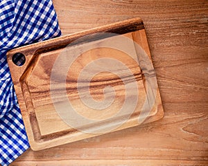 Empty cutting board on blue and white checkered fabric or napkin on rustic wood background.