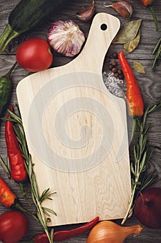 An empty cutting board on a wooden table surrounded by vegetable