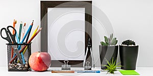 Empty dark photo frame, succulents in dark pots, colored pencils, office supplies, red apple on a white background. Desktop MockUp
