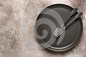 Empty dark plate with forks on brown rutik background. Top view, flat lay