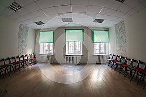 Empty dark room with three windows on wall, chairs standing on the sides and wooden hardfloor, nobody photo