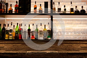 Empty dark wooden bar counter with blur background bottles.