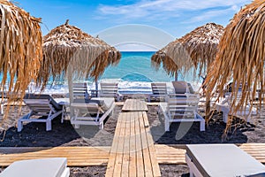Empty deck chairs and umbrellas on the black sand beach in Perissa