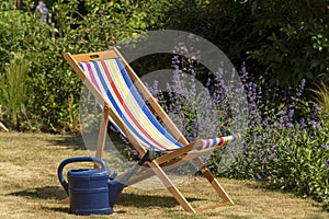 An empty deckchair and watering can in country garden,