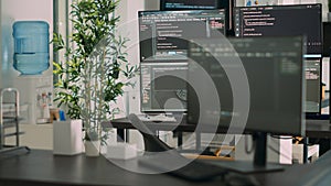 Empty desk with multiple monitors displaying server code and programming language