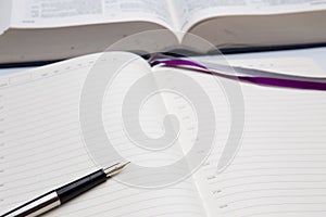 Empty diary or notepad and fountain pen with golden nib closeup, thick opened book in background